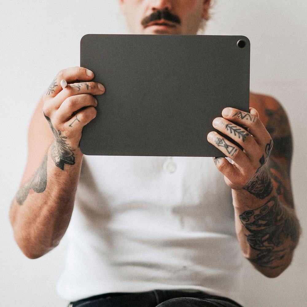 Urban tattooed man in white tank top using digital tablet
