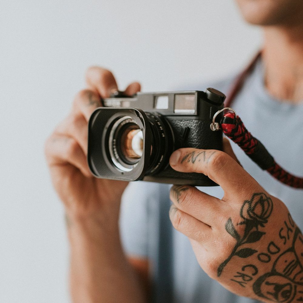 Man with tattooed hands holding an analog camera. 2 OCTOBER 2020 - CHIPPENHAM, UK
