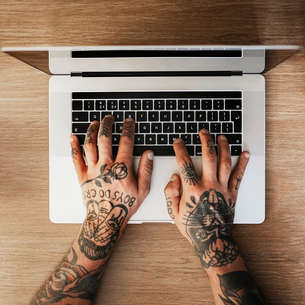 Man with tattooed hands typing on a laptop. 2 OCTOBER 2020 - CHIPPENHAM, UK