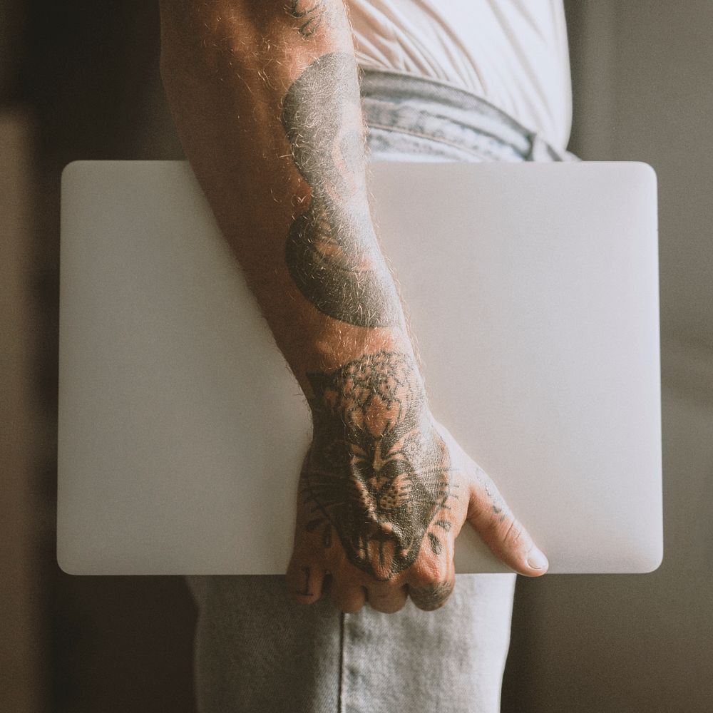 Man with tattooed hands holding a laptop. 2 OCTOBER 2020 - CHIPPENHAM, UK