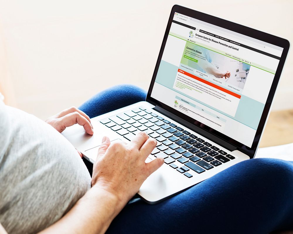 Pregnant woman reading coronavirus information from a laptop mockup with editorial graphic from…