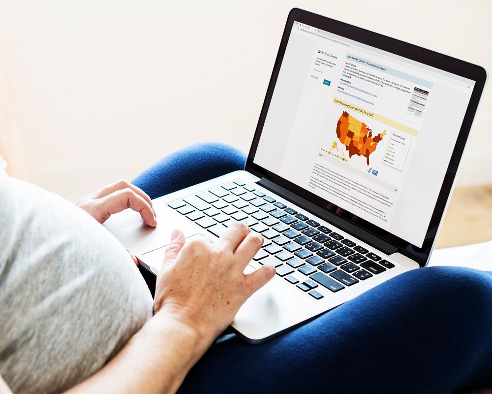 Pregnant woman reading coronavirus updates from a laptop mockup with editorial graphic from…