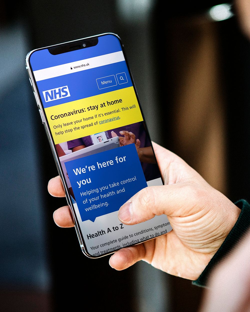 Man reading coronavirus updates from a mobile phone mockup with editorial graphic from https://www.nhs.uk accessed on April…