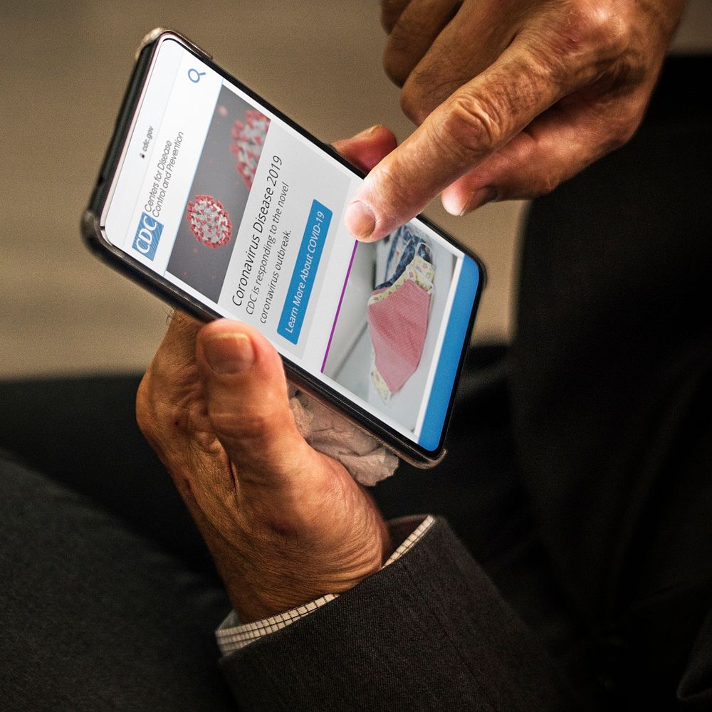 Businessman reading coronavirus updates from a mobile phone mockup with editorial graphic from https://www.cdc.gov accessed…