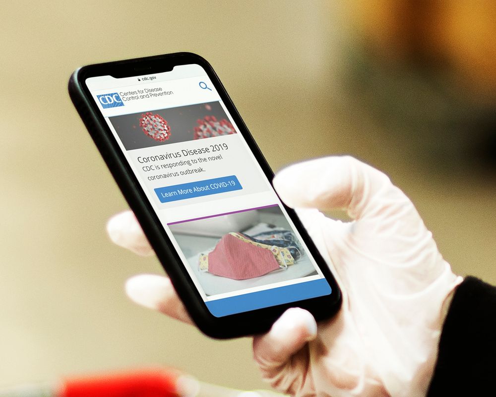 Woman wearing sanitary gloves reading coronavirus updates from a mobile phone mockup with editorial graphic from…