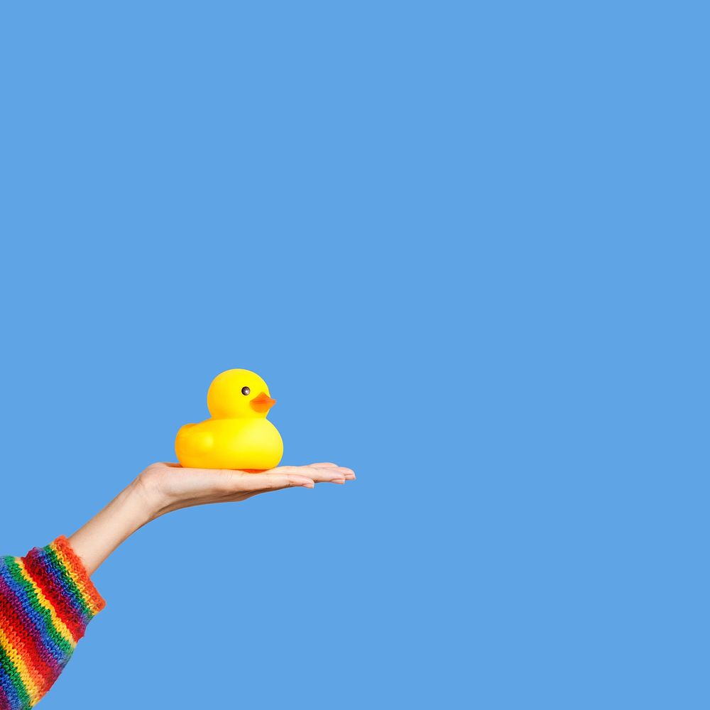 Hand holding a yellow rubber duck on blue background