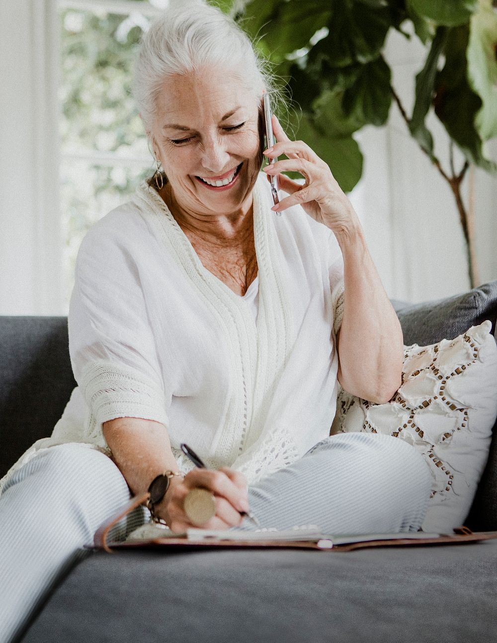 Senior businesswoman on a phone call writing on her planner at home