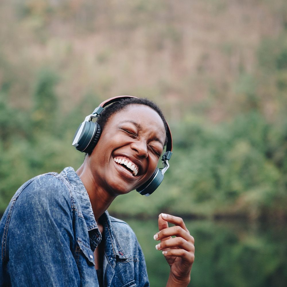 Happy African American woman smiling and enjoying music through her wireless headphones outdoors
