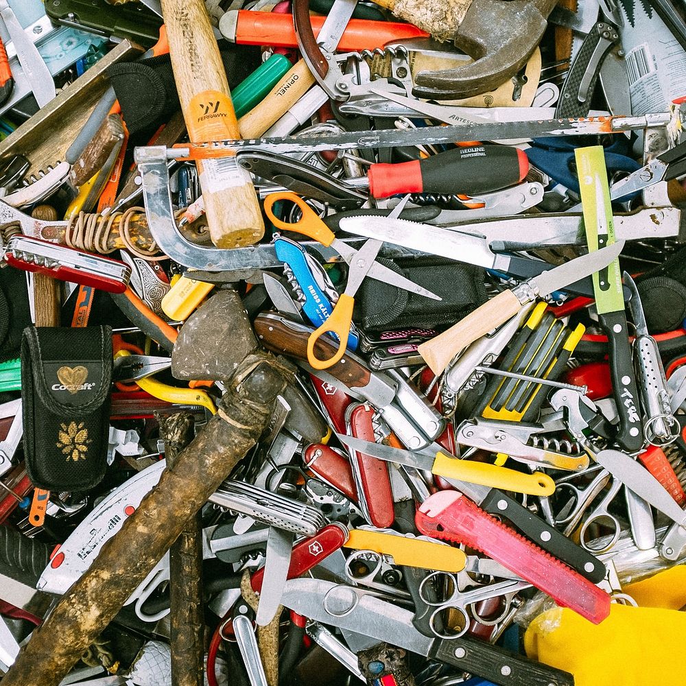 An overhead shot of a heap of scissors, knives, hammers and other tools. Original public domain image from Wikimedia Commons