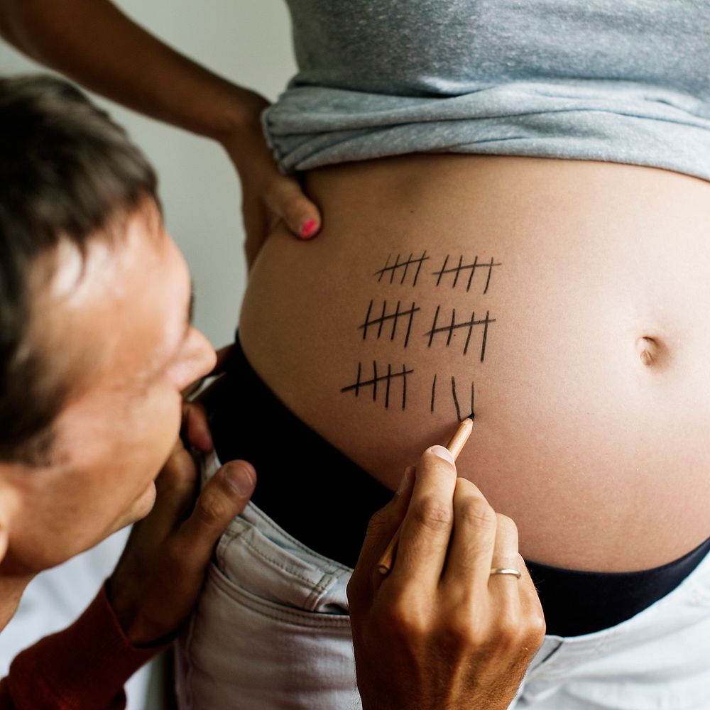 Father marking pregnancy due date on a woman&rsquo;s baby bump
