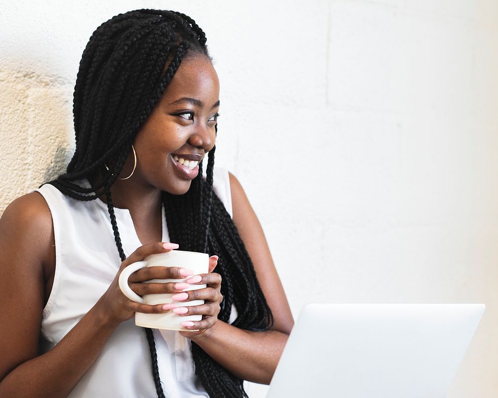 Happy black woman holding a cup of coffee sitting by a notebook