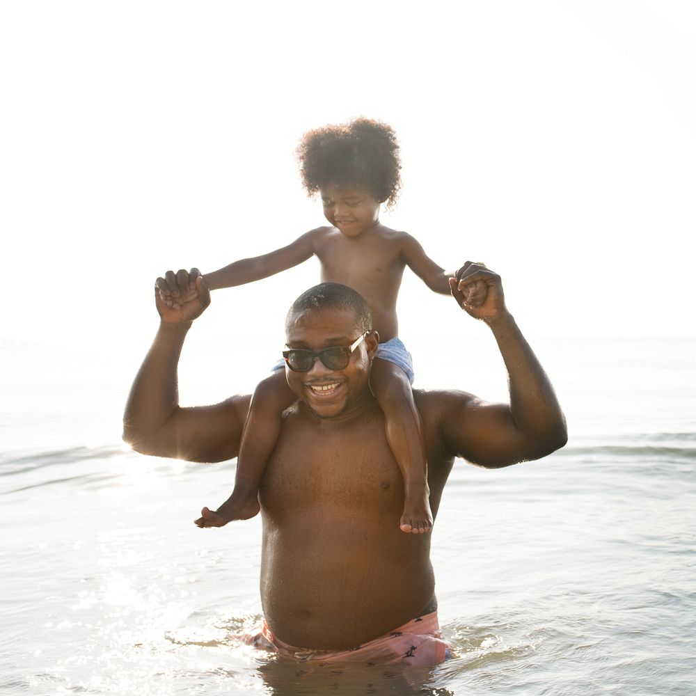 African American dad and son playing piggyback in the sea