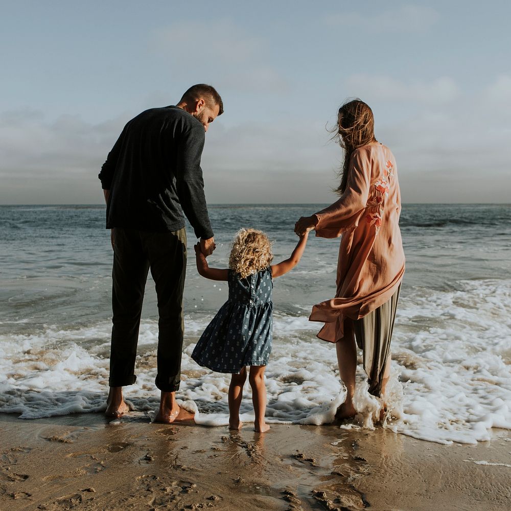 Parents holding daughter's hand at the beach