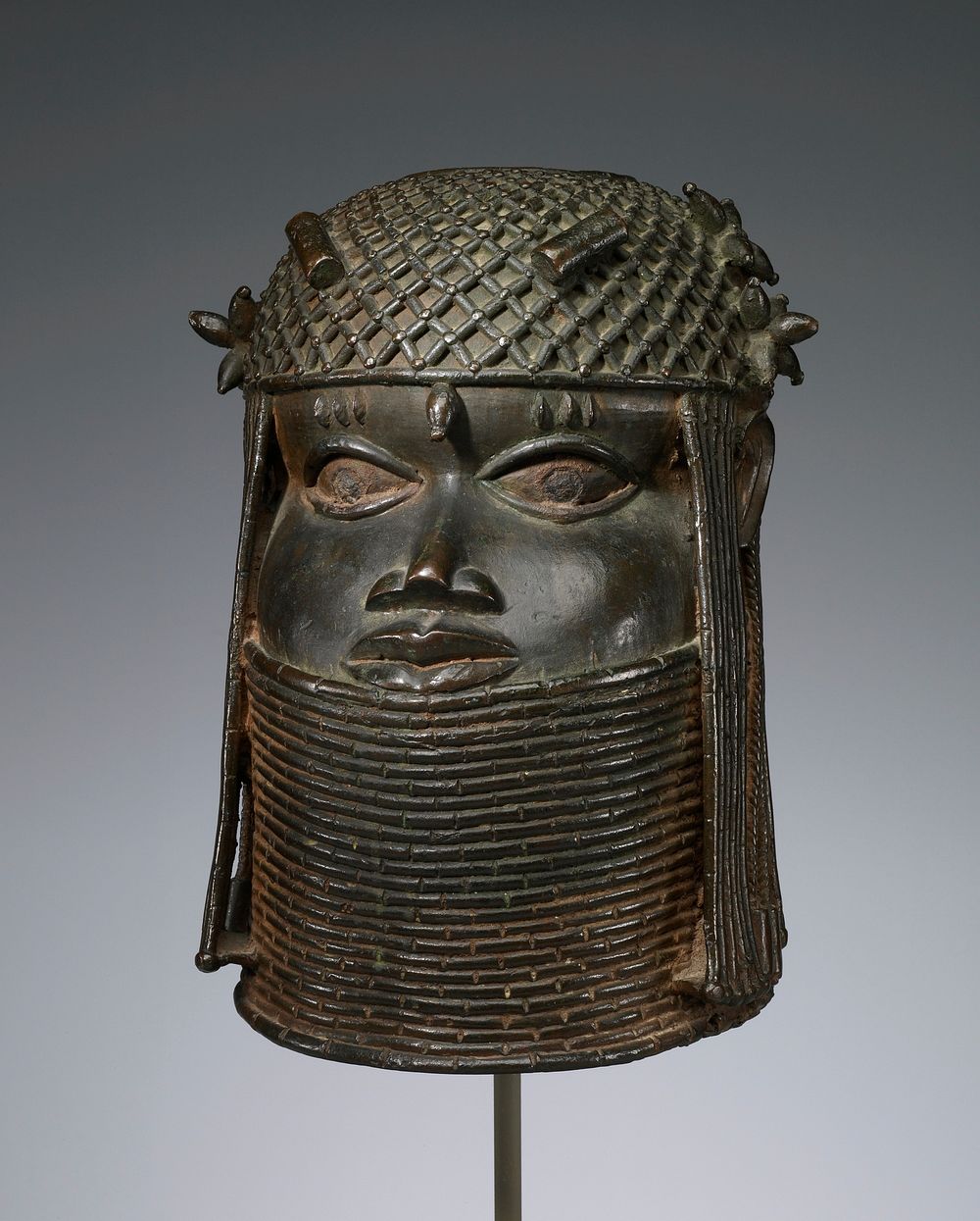 head (male) wearing thick collar up to lower lip; openwork caplike headdress with hanging braids and beaded cords around…