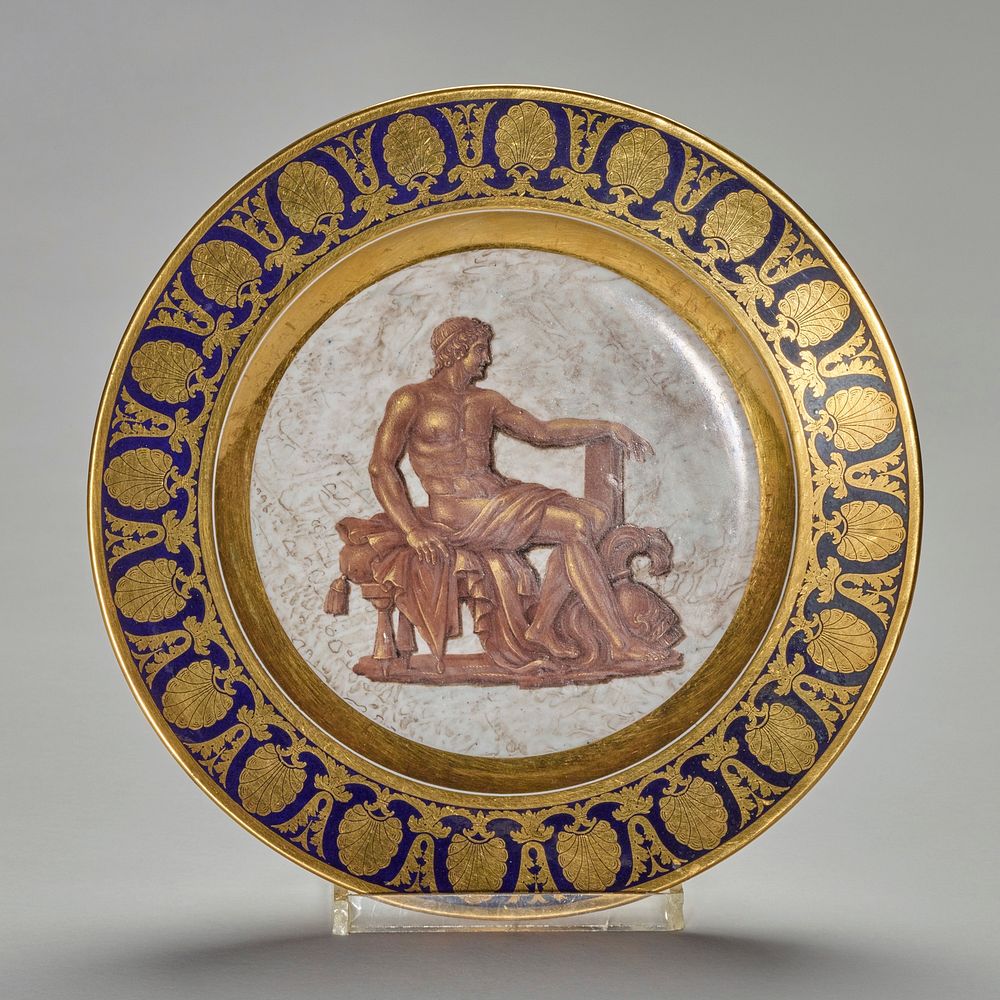 plate, ceramic-porcelain, dark blue with gold border, brown and gold seated figure with helmet at his feet in center agianst…