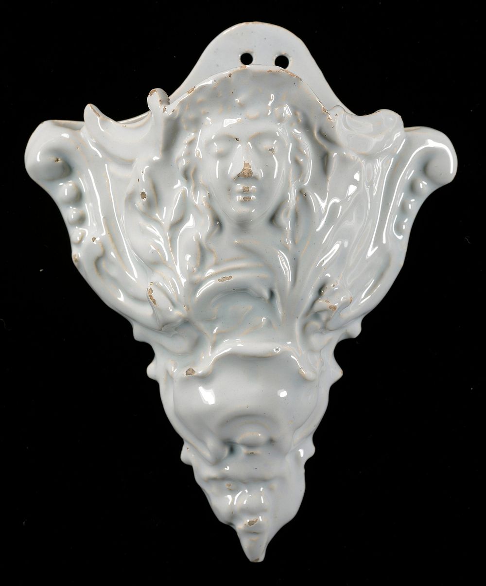white tin glazed wall pocket with molded relief mask; faces at top center and at point on bottom; vines around face at top;…