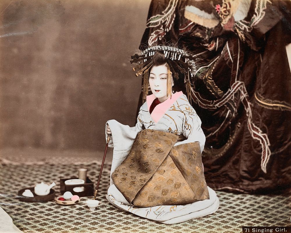 Seated girl wearing headdress with gold tassels and light blue pendants, light blue and gold kimono and tan obi; teaware on…