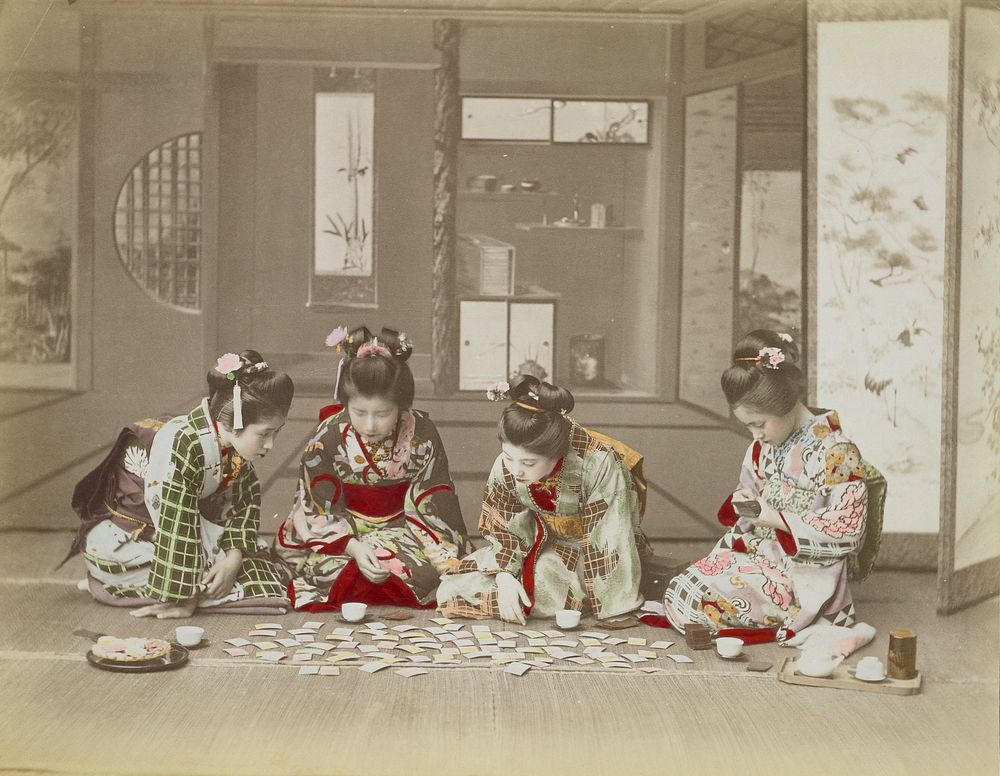 Four seated girls wearing traditional Japanese costumes, looking at pastel-colored cards laid out in front of them on floor…