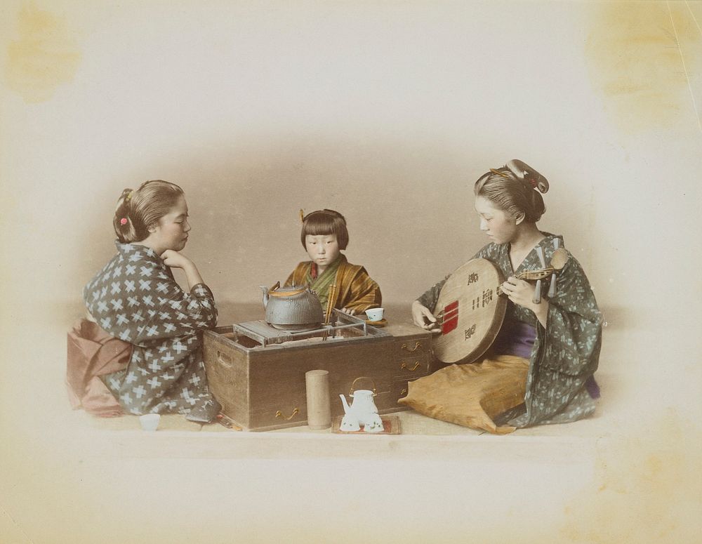 Two young women and a little girl seated around a tea caddy or brazier, with teakettle in center; woman at right plays a…