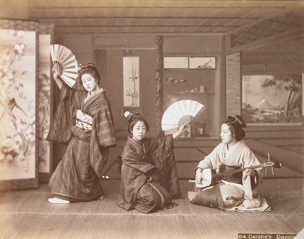 three young women in an interior; seated woman at right plays a shamisen; two other young women with fans and wearing dark…