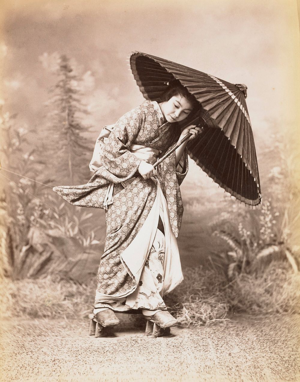 Young woman dressed in patterned kimono, holding a parasol and wearing shoes similar to "geta" sandals but with an enclosed…