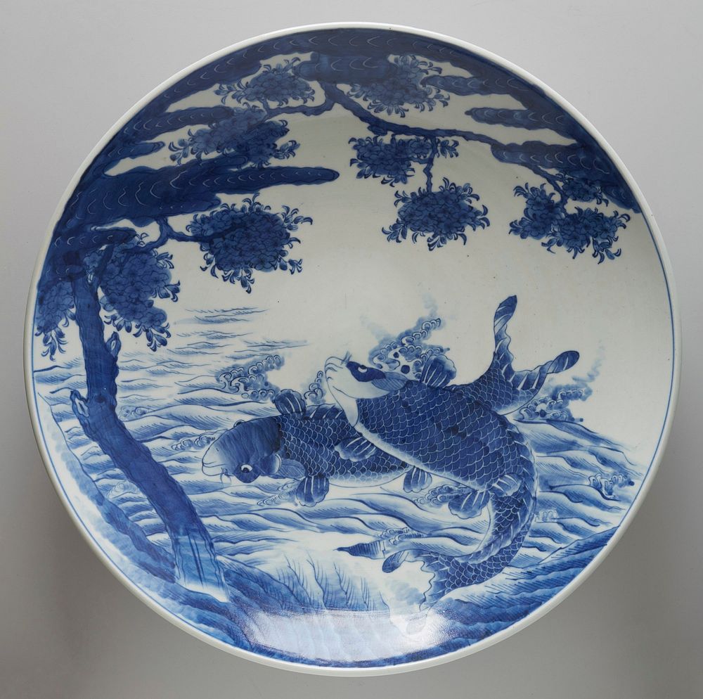 Very large dish with wide ring foot; blue and white; decorated with pair of carp jumping out of water beneath a blooming…