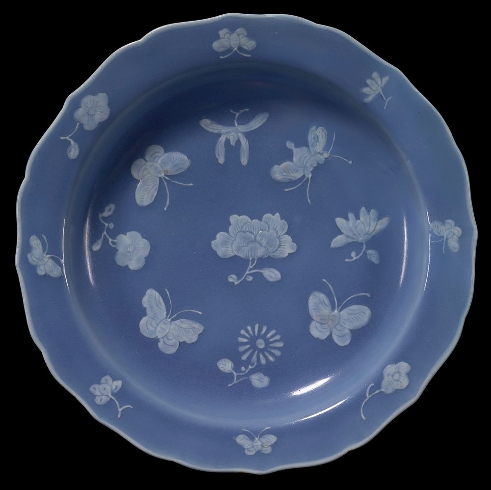 shallow bowl shape; ring foot; heavy base; sloping rim with scalloped edge; medium blue glaze with white flowers and…