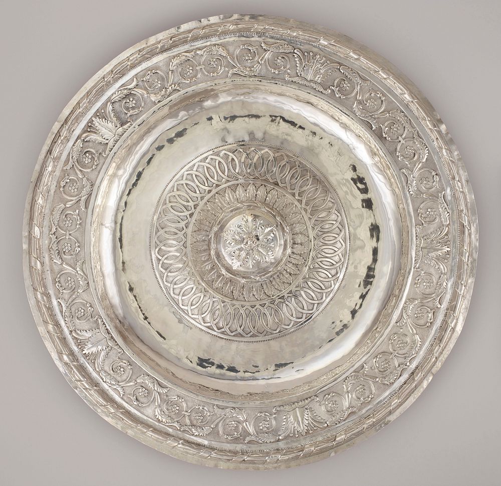 large, thin, round silver platter; central three-dimensional applied large flower form with five petals and cluster of six…