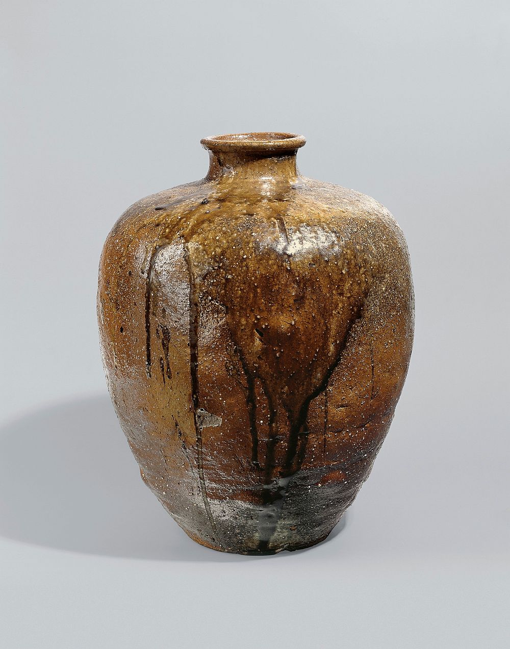 large, rust-colored jar with dripping brown and tan over glaze; narrow base widening to top with graceful, short neck and…