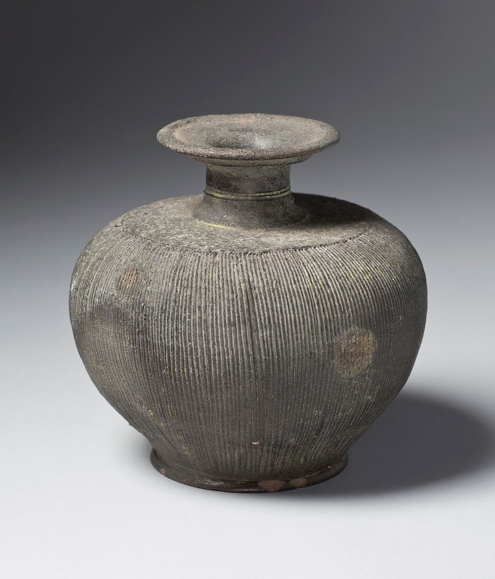 black stoneware decorated with close, thin vertical incised lines around body; squat shape with flat shoulder, short neck…