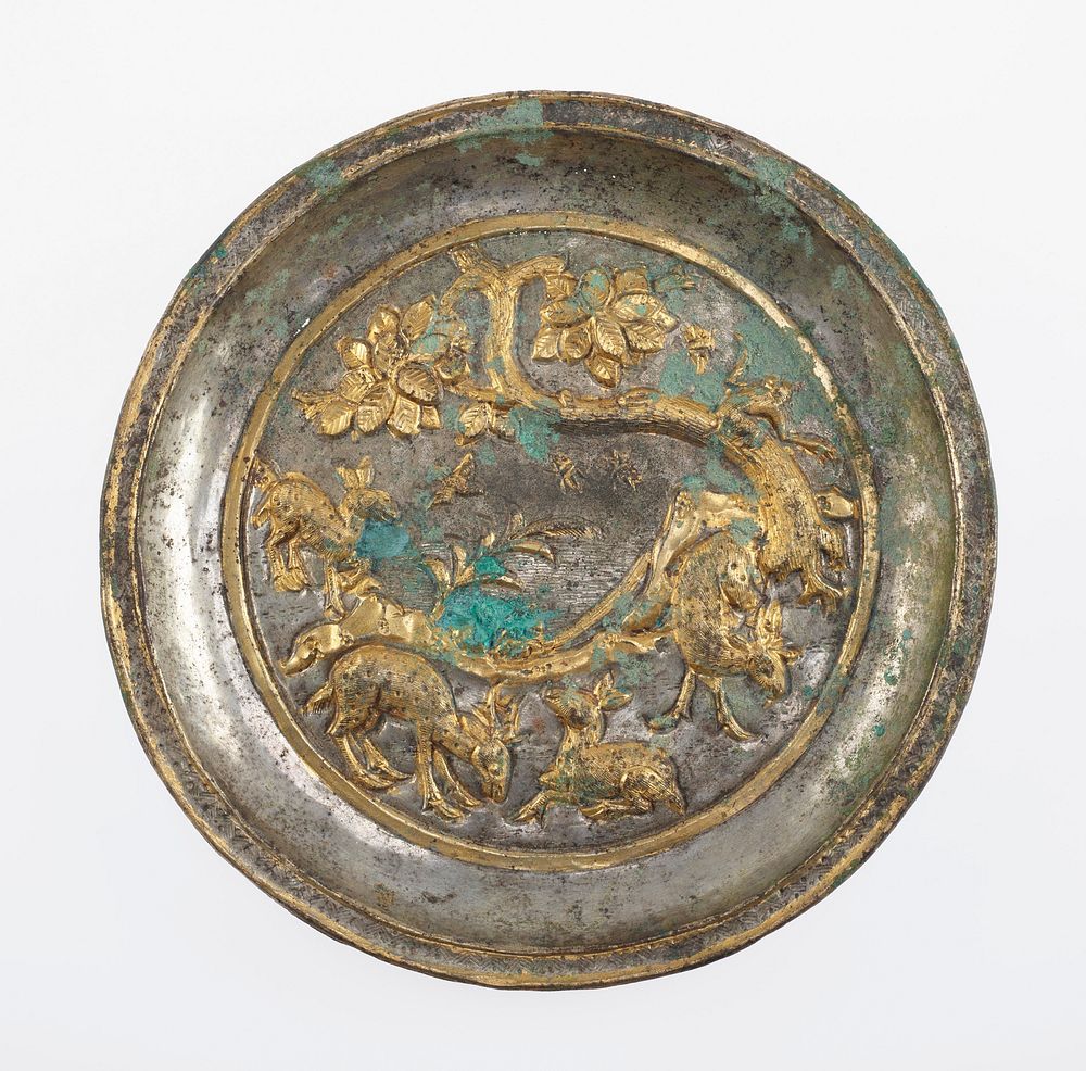 small silver dish with raised gold colored decoration of grazing deer, mountains, and bent tree with a monkey; gold band…