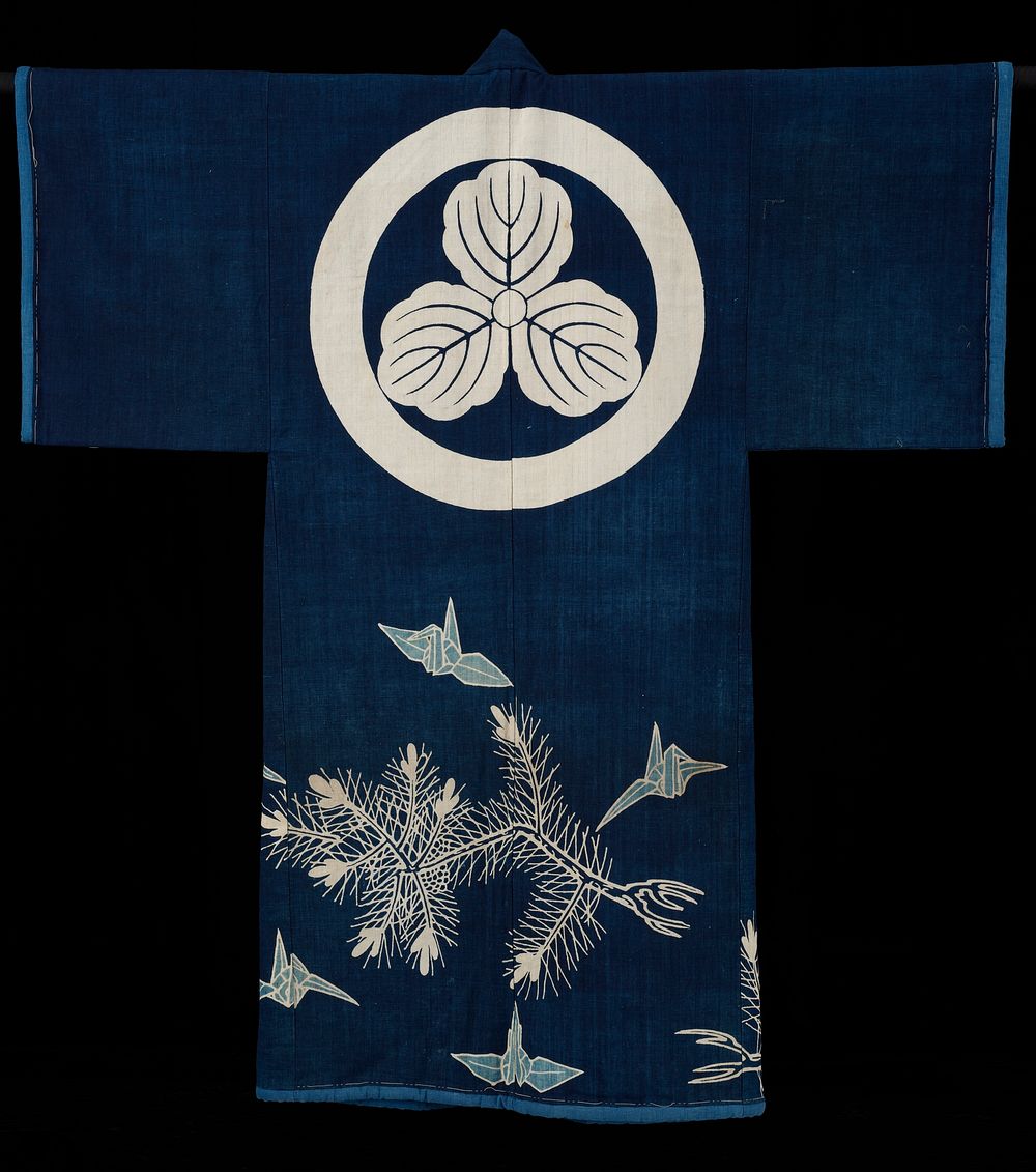 Coverlet in the shape of a kimono; indigo field decorated with cranes and pines and a large crest or medallion on the top of…