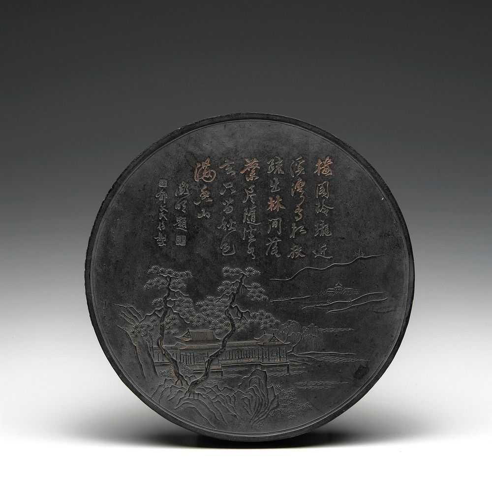circular black ink cake with gilt highlights; landscape with trees, building and water on front, with inscription at top;…