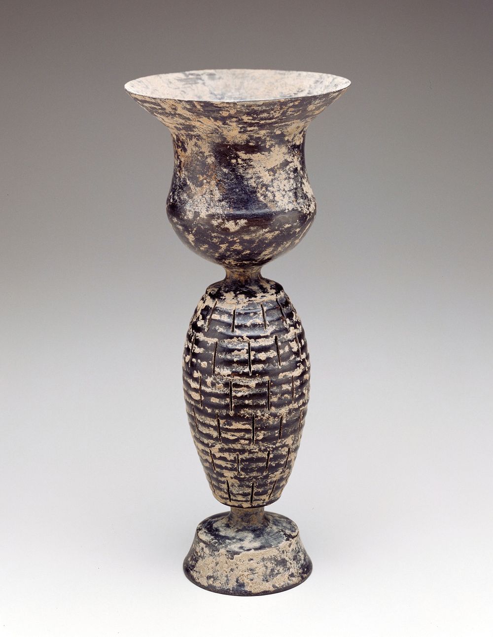 thistle-shaped cup on slender, horizontally ribbed oviform stem pierced with 6 rows of short vertical slits above inverted…
