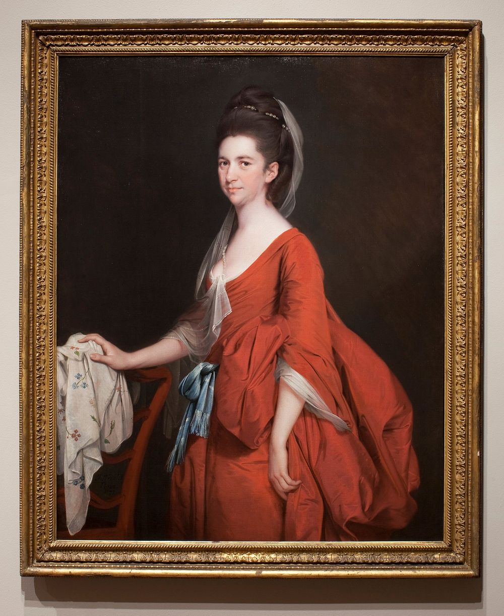 Portrait of a woman in red dress, cut low at the neck, with blue sash; white muslin veil falling from her hair; resting her…