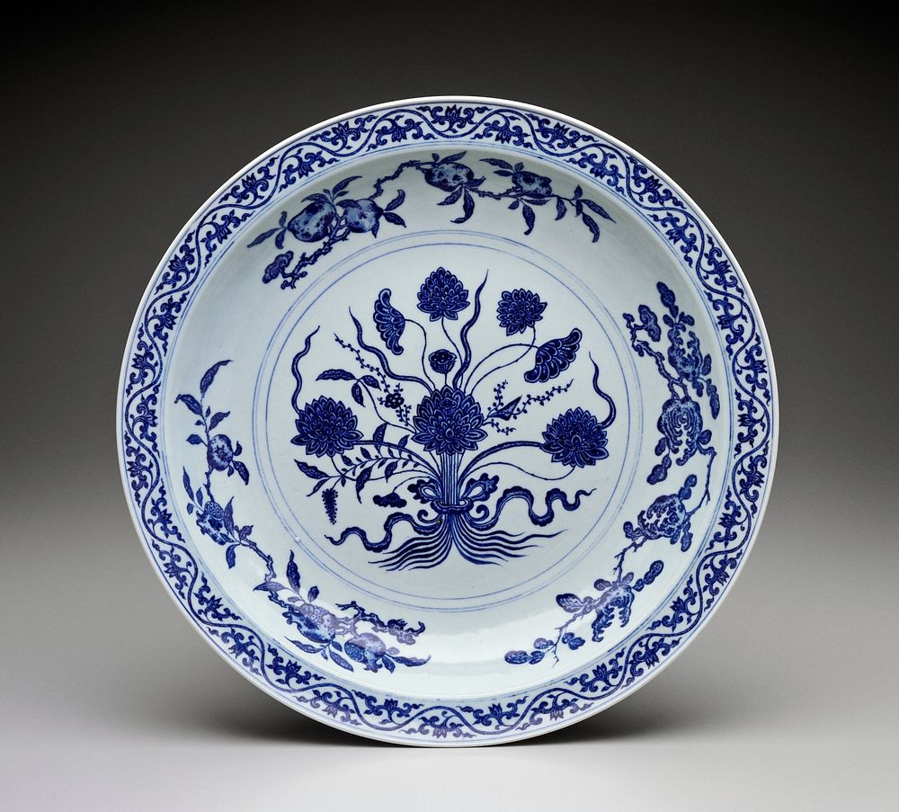 Blue and white bowl with small lip; bouquet of lotus flowers at center with fruits on stems around edge; chased foliage on…