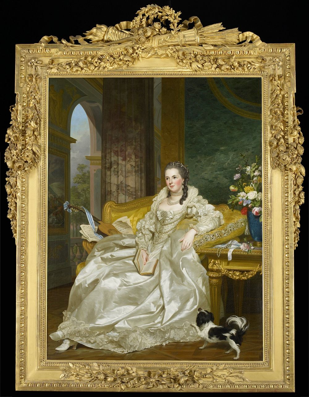 woman wearing a white satin gown trimmed with lace and pearls, holding a book, and seated on a yellow sofa; woman wears…