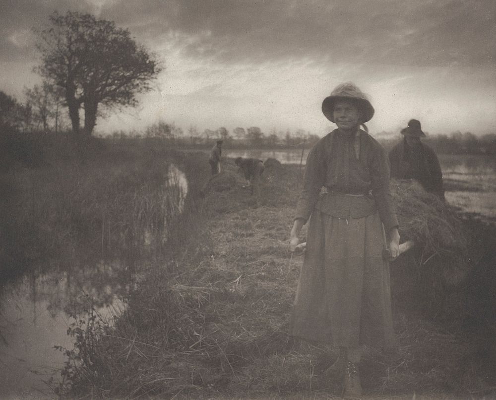 woman wearing a hat and ankle-length skirt, pulling a barrow of hay; man behind barrow; two other figures in middle ground…