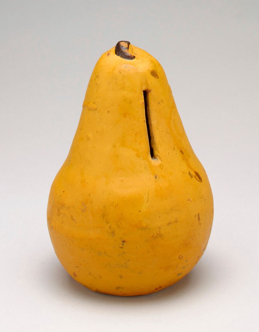 ceramic bank shaped and painted to resemble a yellow pear with brown stem; coin slot in neck of pear. Original from the…