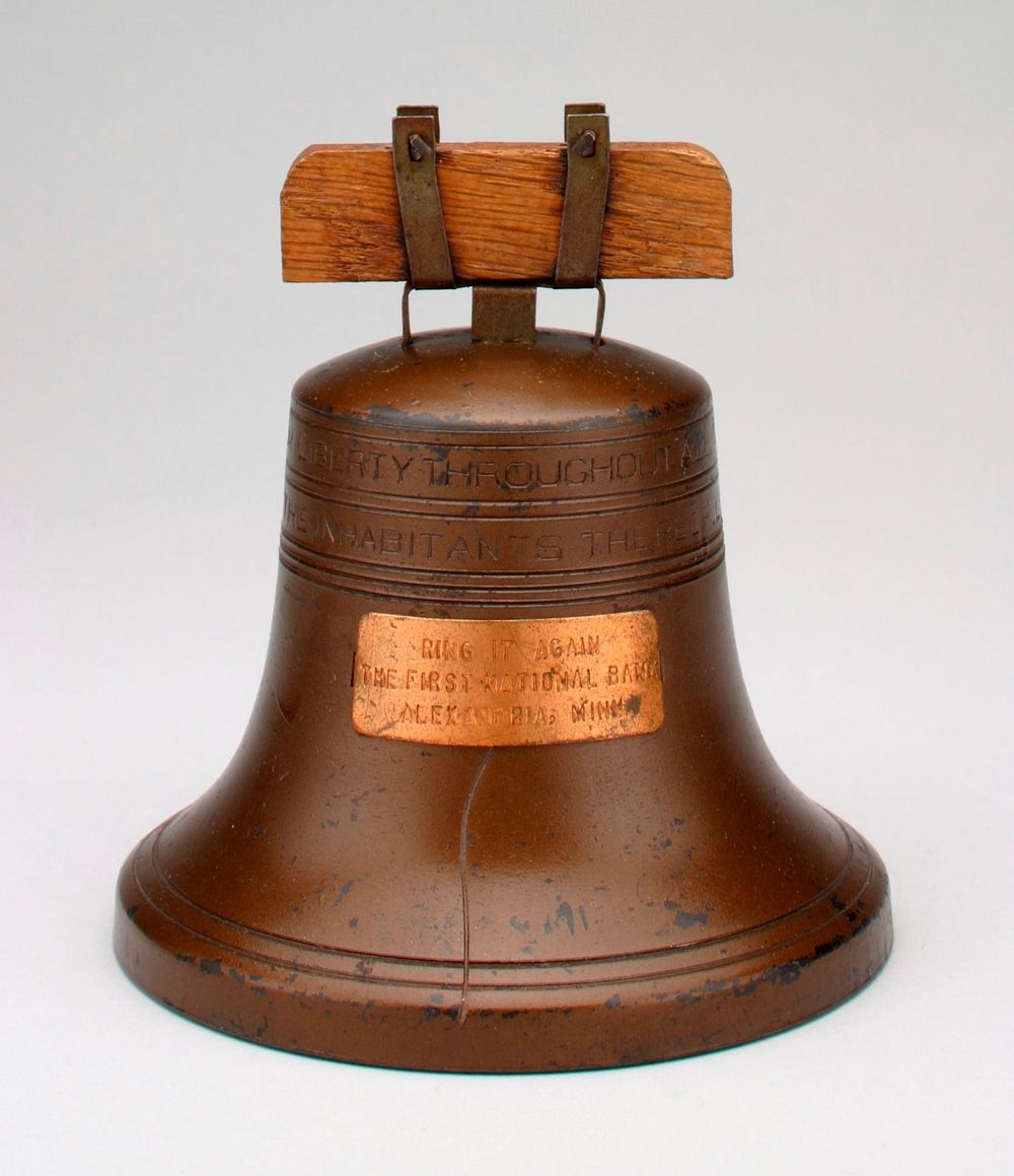 copper colored Liberty Bell with plaque on front: "Ring it Again/ The First National Bank/ Alexandria, Minn."; around top is…
