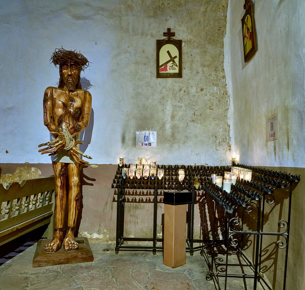                         Votive candles and religious sculpture at the rear of the El Santuario de Chimayo, a humble but…