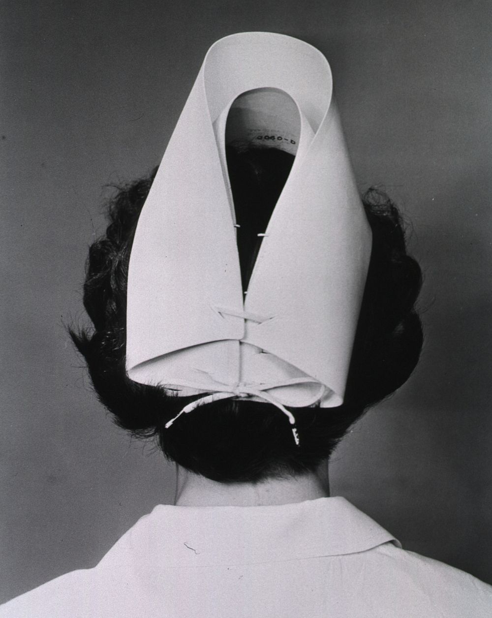 Nurse's Cap. A nurse stand with her back to the camera and is shown from the shoulders up. She models a stripeless nurse's…