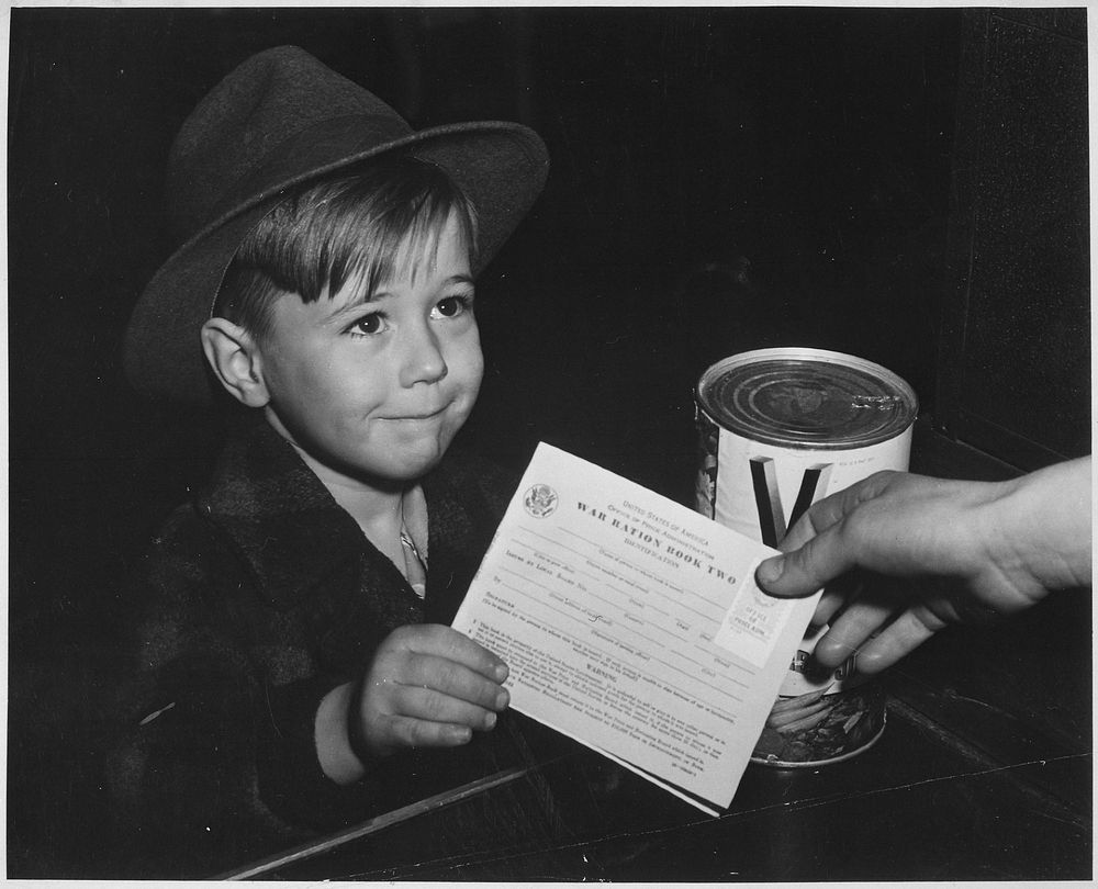 An eager school boy gets his first experience in using War Ration Book Two. With many parents engaged in war work, children…
