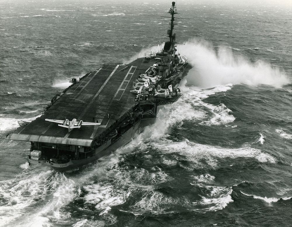 The U.S. Navy aircraft carrier USS Essex (CVA-9) takes spray over the bow while steaming in heavy seas. Essex, with assigned…