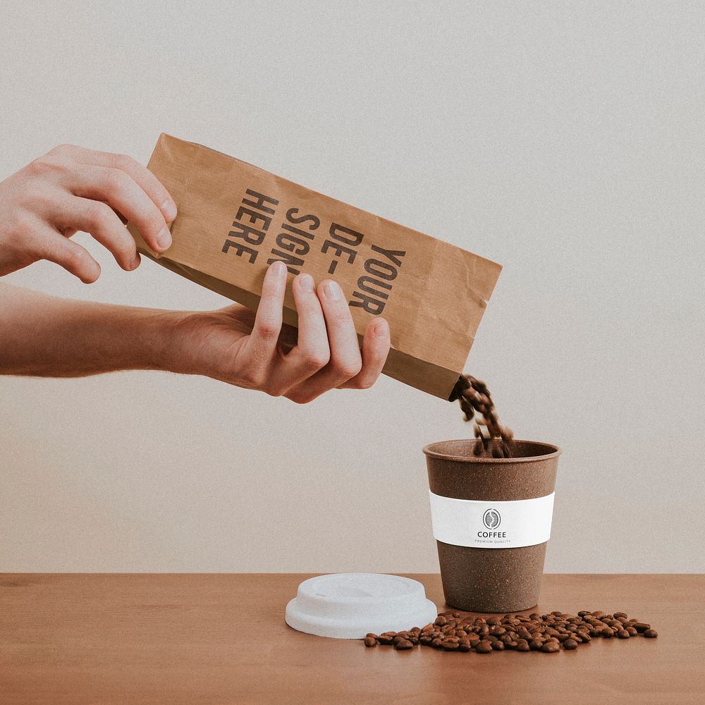 Hand pouring coffee beans from a paper bag into a coffee cup mockup