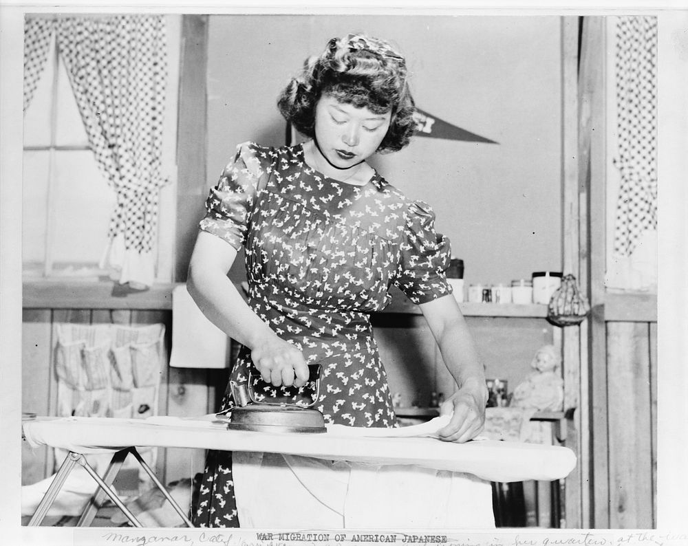 Japanese relocation, California. Ester Naite, an office worker from Los Angeles, is shown operating an electric iron in her…