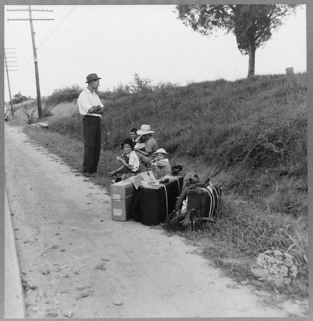 A hitchhiking family waiting along the highway in Macon, Georgia. The father repairs sewing machines, lawn mowers, etc. He…