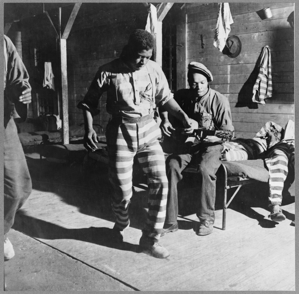 A prisoner dancing while another plays the guitar at a prison camp. Greene County, Georgia. Sourced from the Library of…