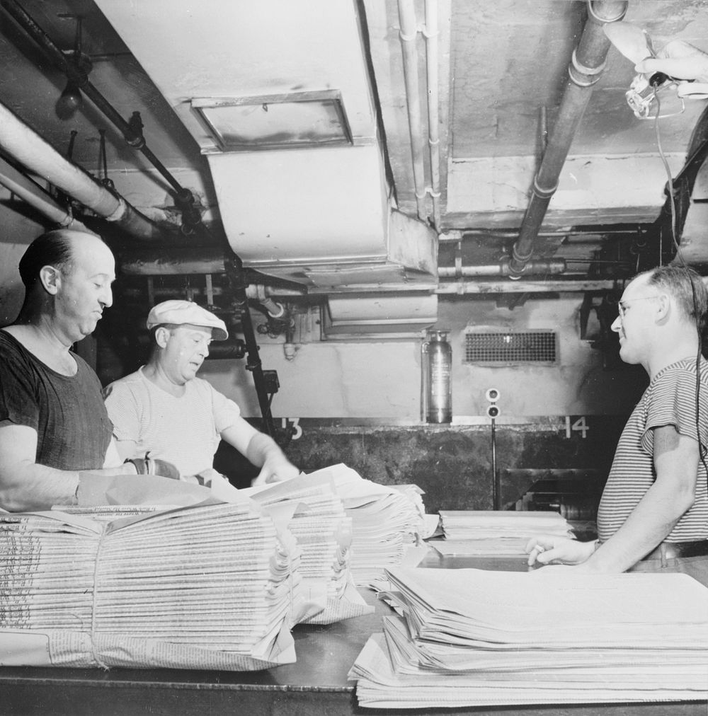 New York, New York. Mailroom of the New York Times newspaper. Papers, delivered from press room on a conveyor, are tied into…