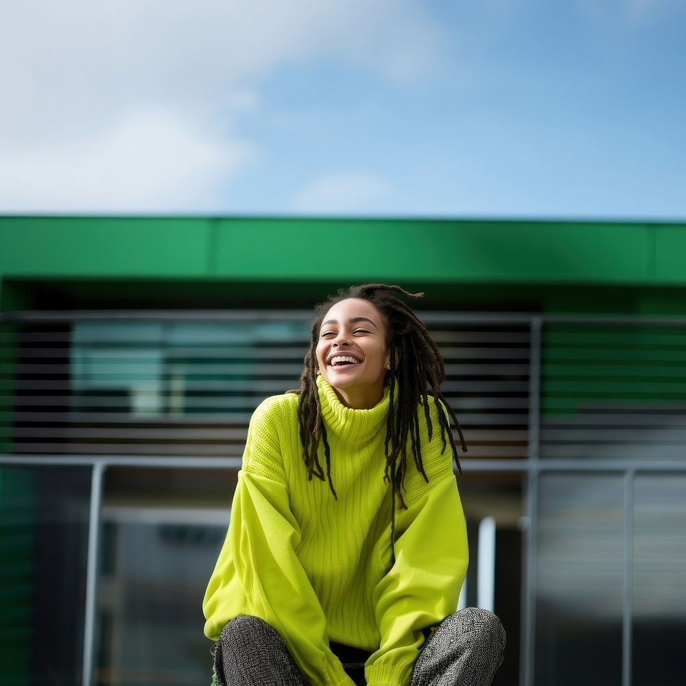 a woman with dreadlocks smiling wearing lime green sweater, playful poses, close up, outdoor city, cool.  